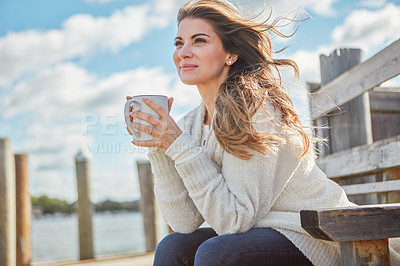 Buy stock photo Shot of a beautiful young woman enjoying a warm beverage while relaxing on a bench at a lake
