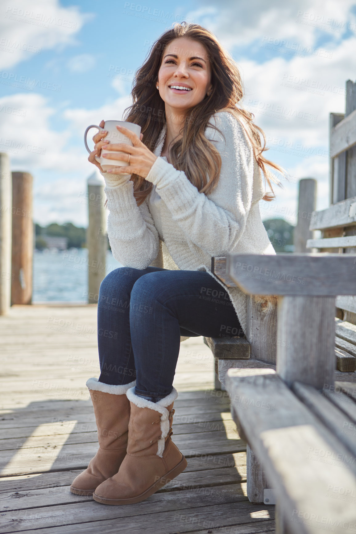 Buy stock photo Shot of a beautiful young woman enjoying a warm beverage while relaxing on a bench at a lake