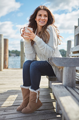 Buy stock photo Shot of a beautiful young woman enjoying a warm beverage while relaxing on a bench at a lake