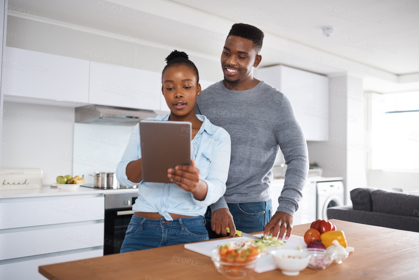 Buy stock photo Shot of a couple looking at something on a digital tablet while cooking