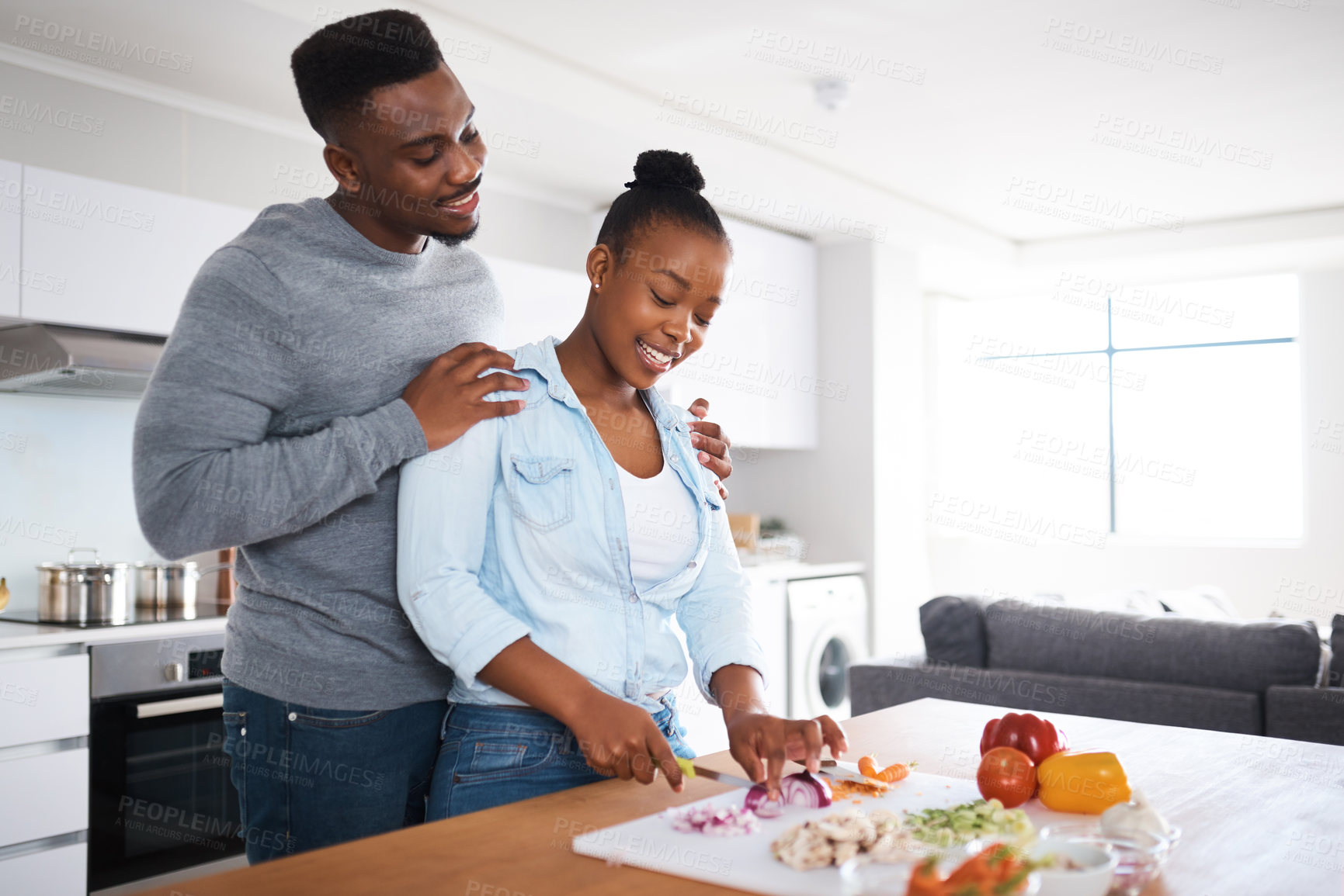 Buy stock photo Shot of a man embracing his wife from behind while she's with chopping vegetables