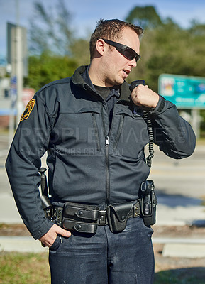 Buy stock photo Cropped shot of a handsome young policeman radioing in with headquarters