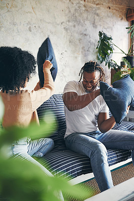 Buy stock photo Shot of a young couple having a pillow fight while relaxing together on a sofa at home