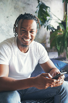Buy stock photo Portrait of a young man using a cellphone while relaxing on a sofa at home