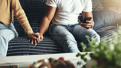 Buy stock photo Closeup shot of an unrecognisable man holding his partner's hand while using a cellphone at home