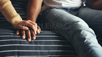 Buy stock photo Closeup shot of an unrecognisable couple holding hands while sitting together on a sofa at home