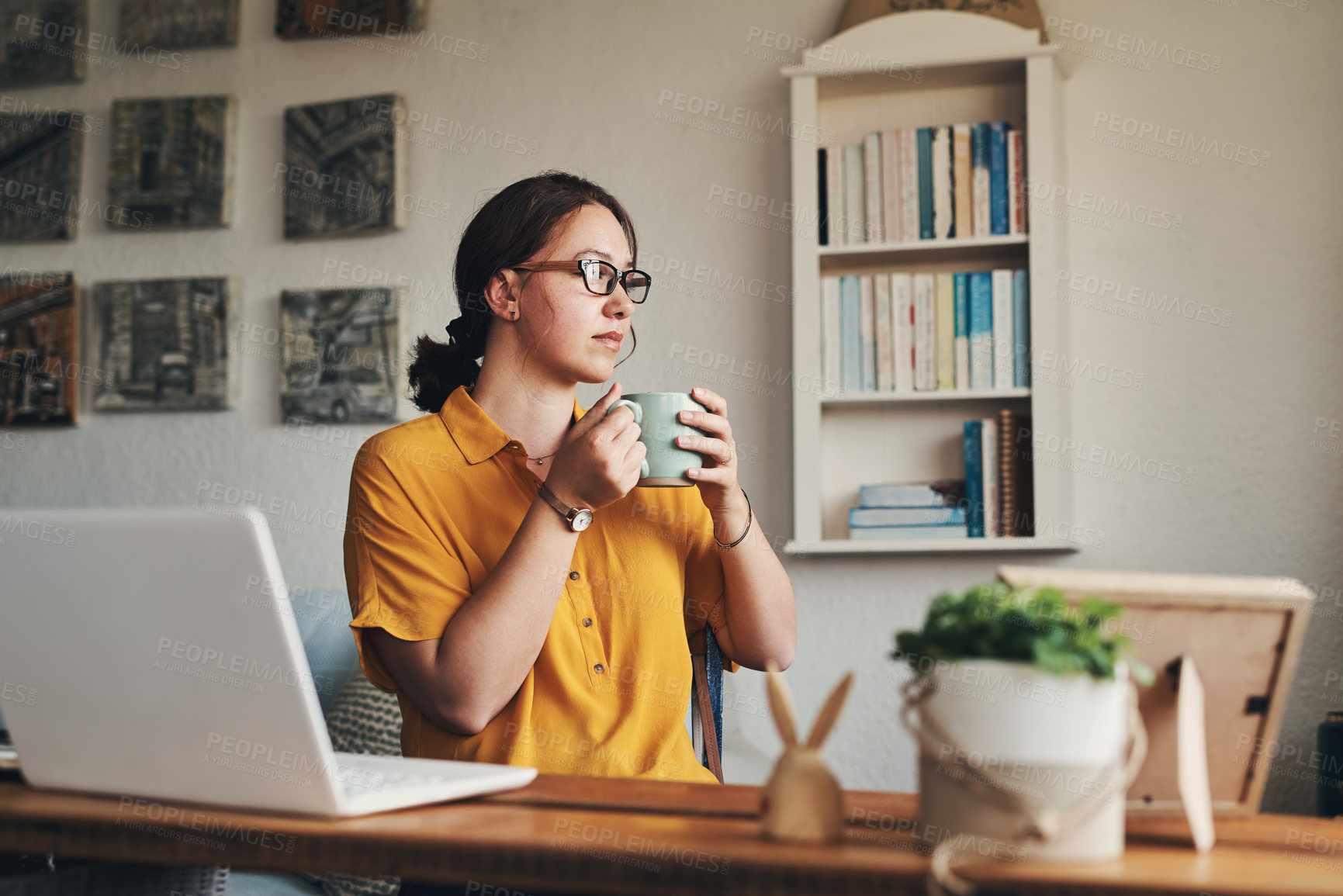 Buy stock photo Shot of a young woman having coffee and looking thoughtful while working from home