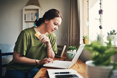 Buy stock photo Shot of a young woman using a laptop and credit card while working from home