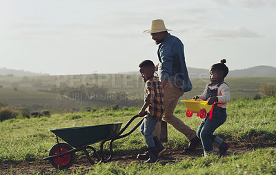 Buy stock photo Man, son and daughter working on a farm with a wheel barrow for agriculture in the countryside. Family, farming and children work in the outdoor of a rural environment with joy and fun for learning.