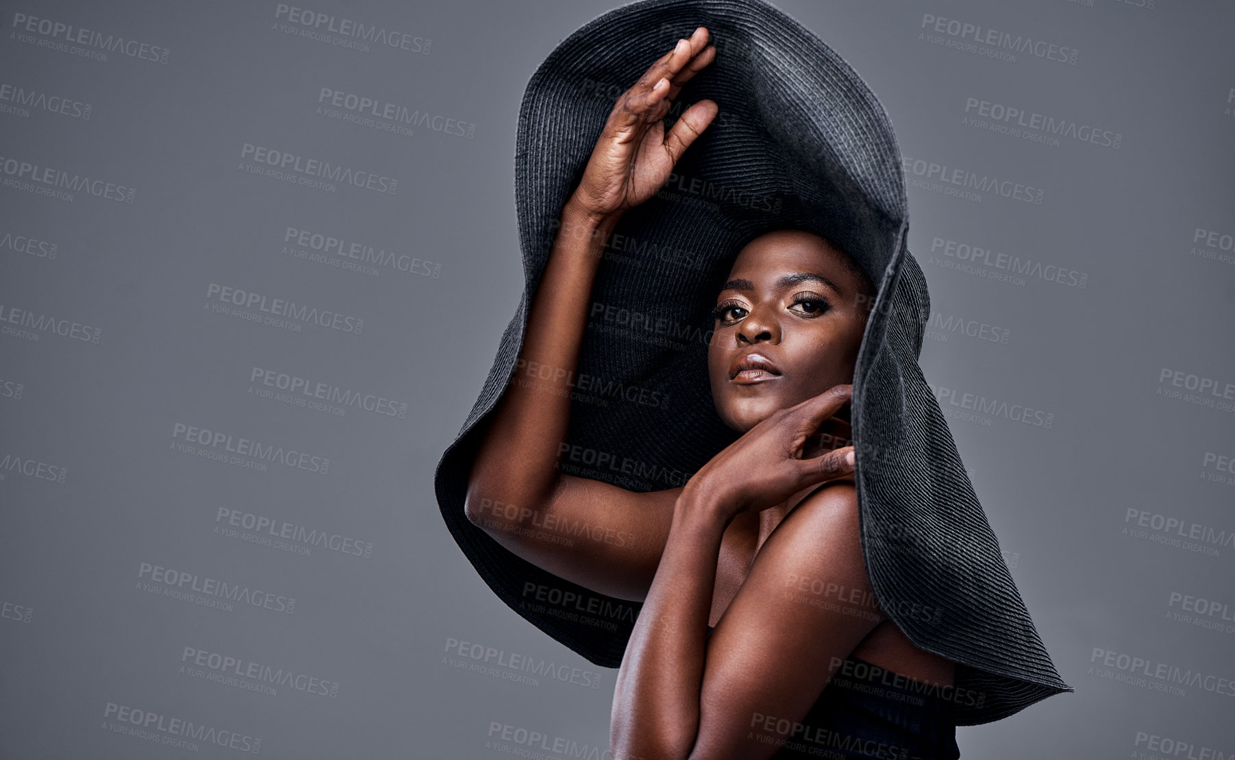 Buy stock photo Shot of a young woman wearing a oversized sunhat against a grey background