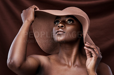 Buy stock photo Shot of a beautiful young woman wearing a hat while posing against a brown background