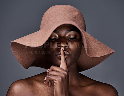Buy stock photo Shot of a young woman wearing a hat and posing with her finger on her lips against a grey background