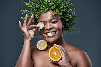 Buy stock photo Shot of a woman wearing a leaf wreath while holding cucumber, lemon and an orange against her skin