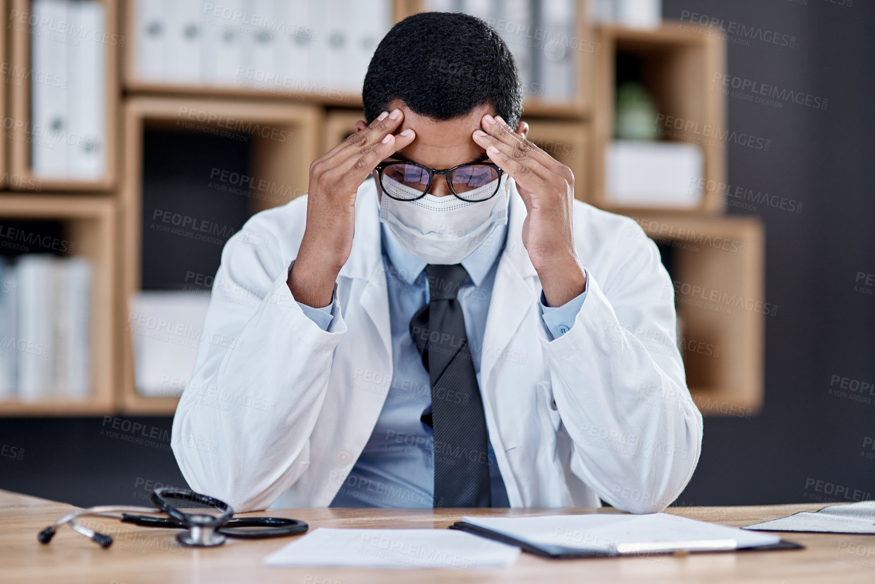 Buy stock photo Shot of a young doctor looking stressed out while working in his office