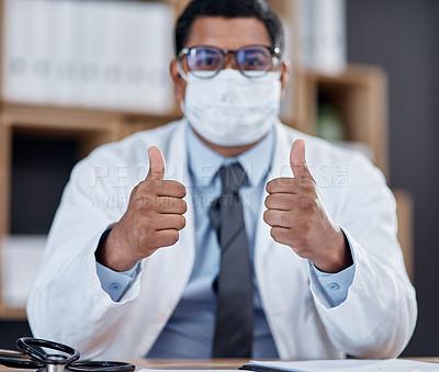 Buy stock photo Portrait of a young doctor wearing a face mask and showing thumbs up in his office
