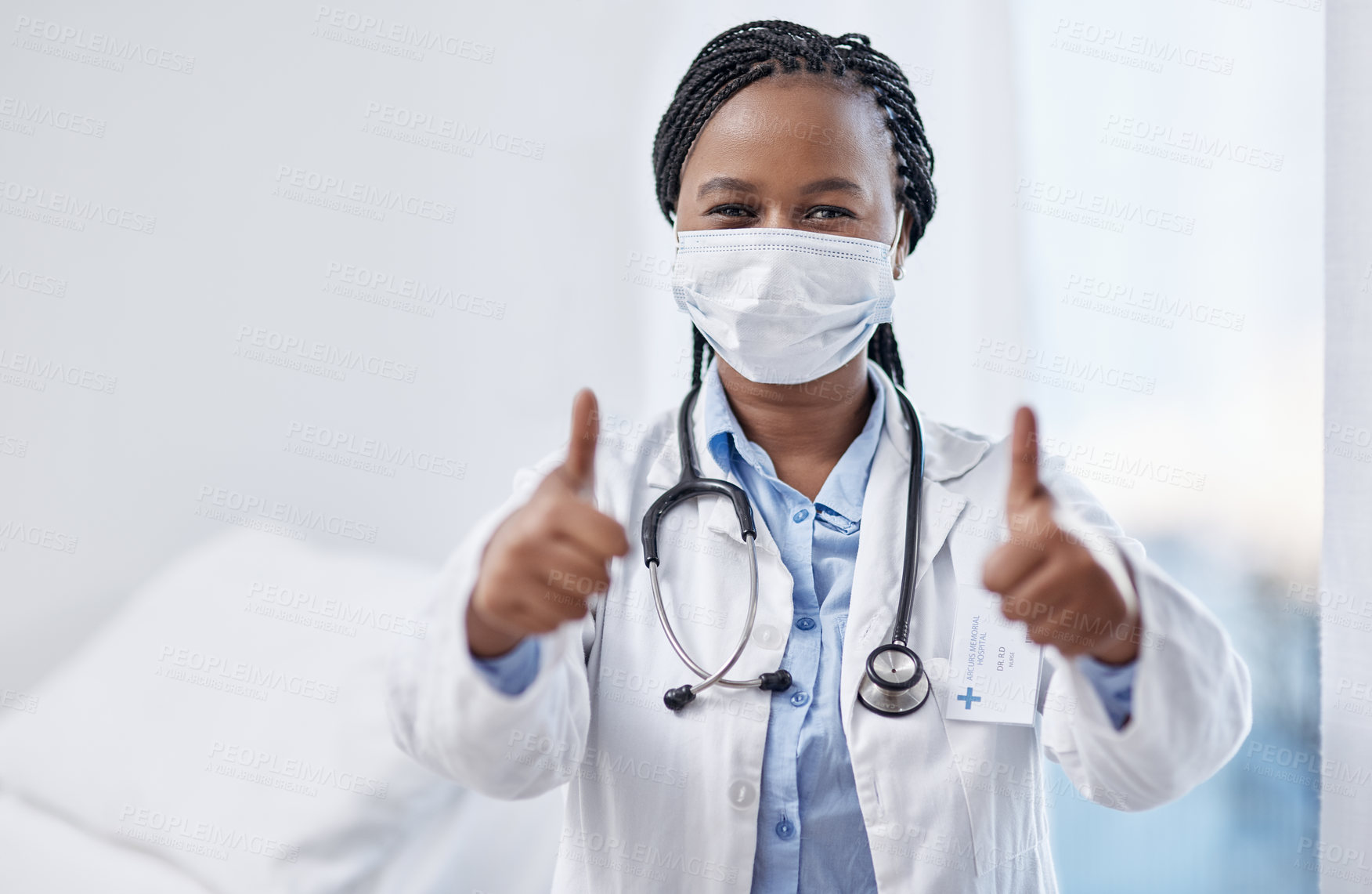 Buy stock photo Portrait of a young doctor wearing a face mask and showing thumbs up in a hospital