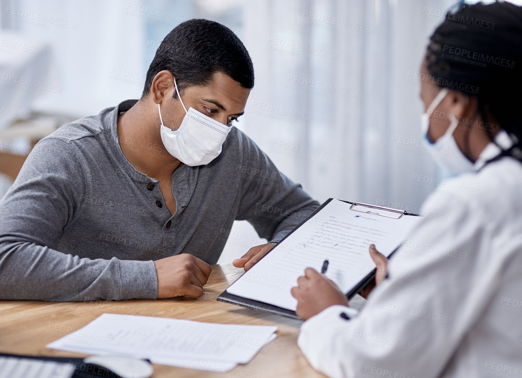 Buy stock photo Shot of a young man going through paperwork during a consultation with a doctor