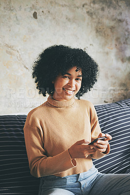 Buy stock photo Portrait of a young woman using a cellphone while relaxing on a sofa at home