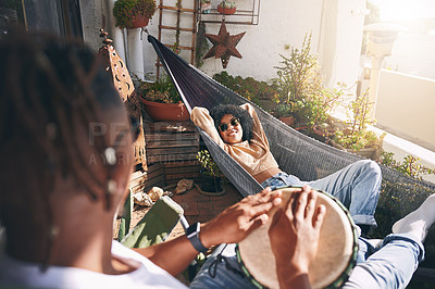 Buy stock photo Shot of a young woman relaxing on a hammock while listening to her boyfriend play drums