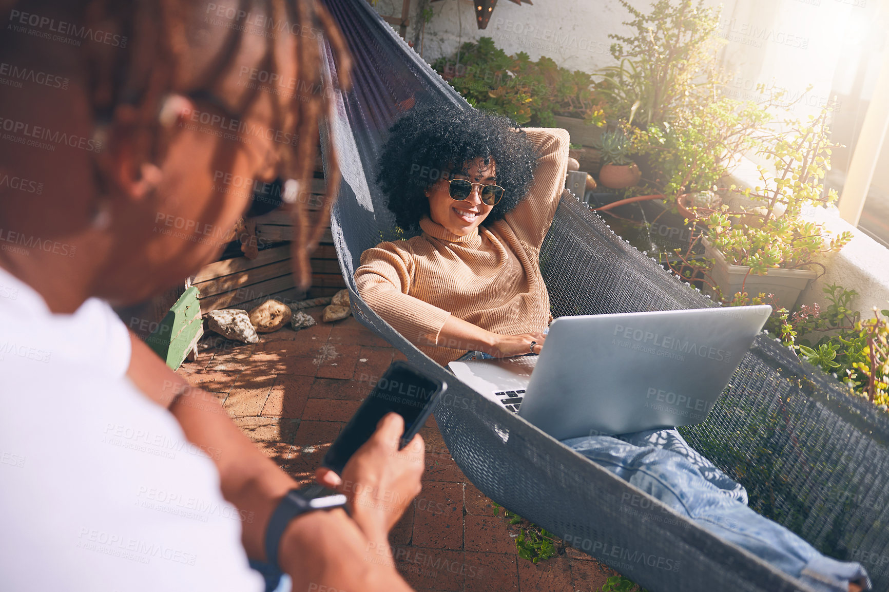 Buy stock photo Shot of a young woman using a laptop and relaxing on a hammock while her boyfriend uses a cellphone