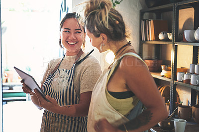Buy stock photo Shot of two young women using a digital tablet while working together in a pottery studio