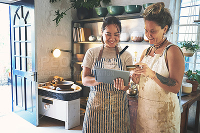 Buy stock photo Shot of two young women using a digital tablet and credit card while working together in a pottery studio