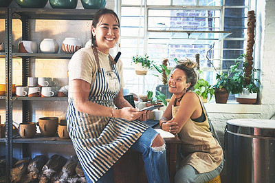 Buy stock photo Shot of two young women using a digital tablet while working together in a pottery studio