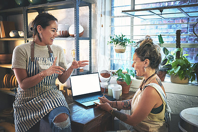 Buy stock photo Shot of two young women using a laptop while working together in a pottery studio
