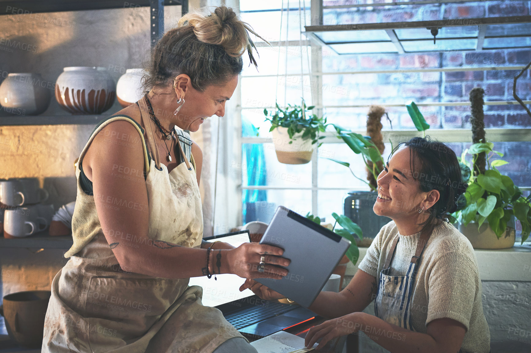 Buy stock photo Shot of two young women using a digital tablet while working together in a pottery studio