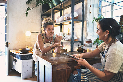 Buy stock photo Shot of two young women using a digital tablet during a meeting in a pottery studio