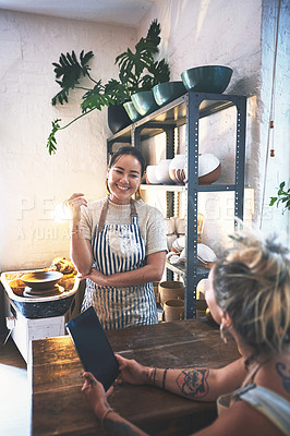 Buy stock photo Shot of two young women using a digital tablet during a meeting in a pottery studio