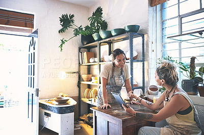 Buy stock photo Shot of two young women using a digital tablet during a meeting in a pottery studio