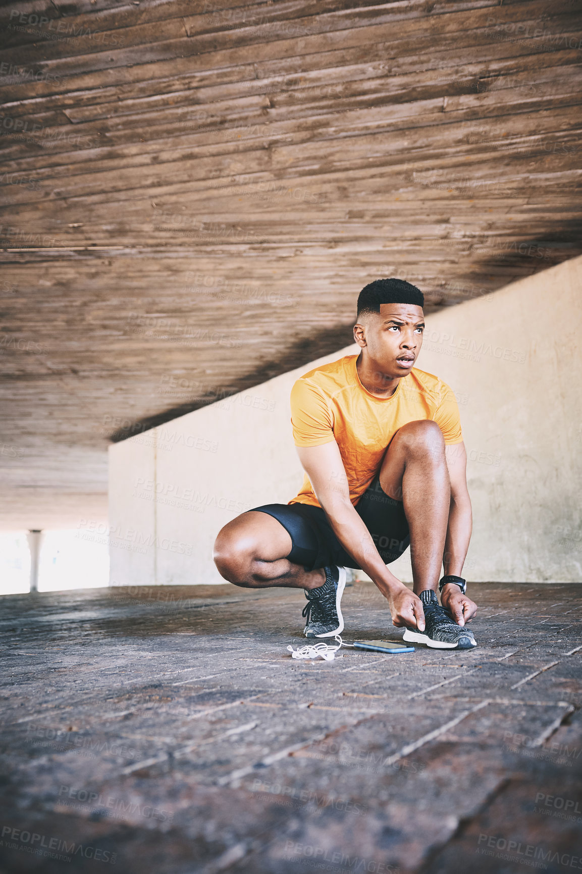 Buy stock photo Shot of a young man tying his shoelaces during a workout against an urban background