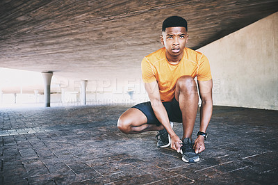 Buy stock photo Shot of a young man tying his shoelaces during a workout against an urban background