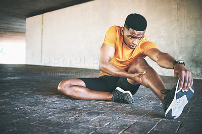 Buy stock photo Shot of a young man stretching during a workout against an urban background