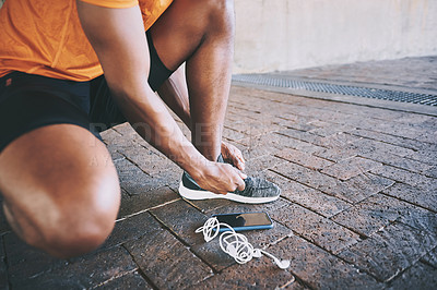 Buy stock photo Cropped shot of a man tying his shoelaces during a workout against an urban background