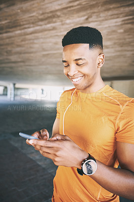 Buy stock photo Shot of a young man using a smartphone and earphones during a workout against an urban background