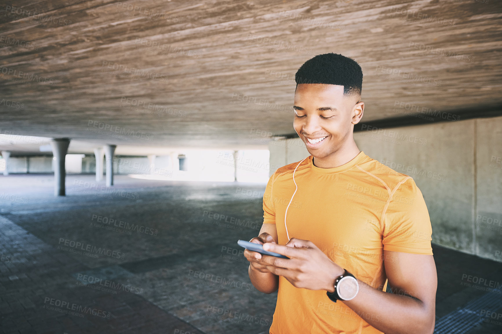 Buy stock photo Shot of a young man using a smartphone and earphones during a workout against an urban background