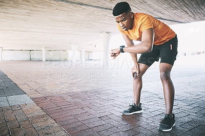 Buy stock photo Shot of a young man looking at his watch during a workout against an urban background