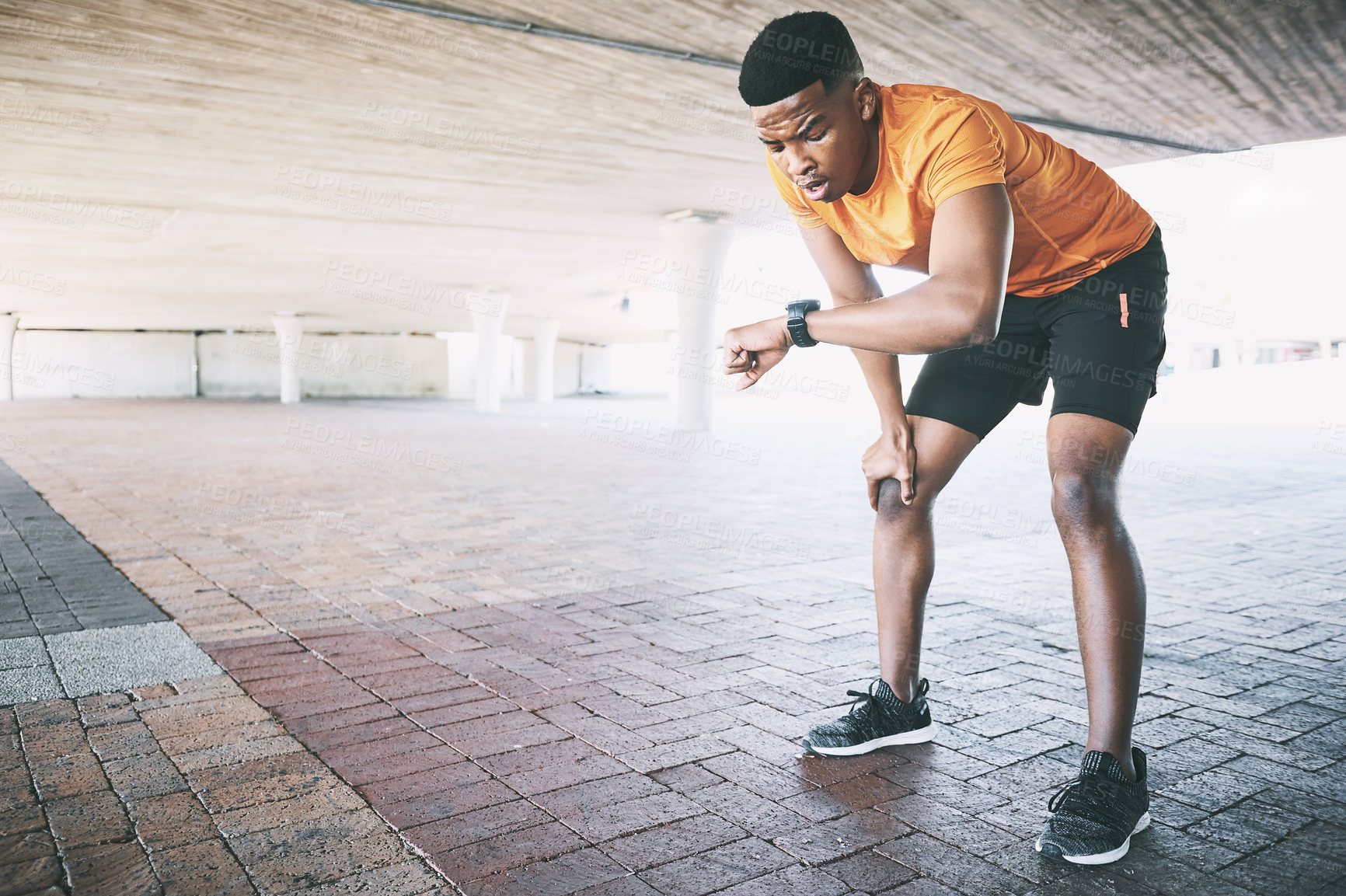 Buy stock photo Shot of a young man looking at his watch during a workout against an urban background