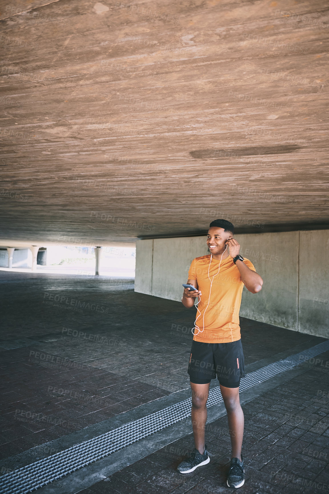 Buy stock photo Shot of a young man using a smartphone and earphones during a workout against an urban background