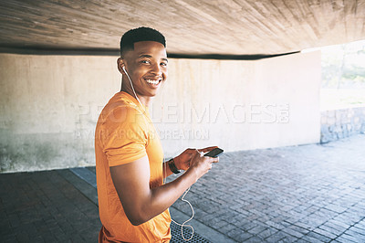 Buy stock photo Portrait of a young man using a smartphone and earphones during a workout against an urban background
