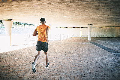 Buy stock photo Rearview shot of a young man going for a run against an urban background