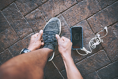 Buy stock photo Cropped shot of a man tying his shoelaces during a workout against an urban background