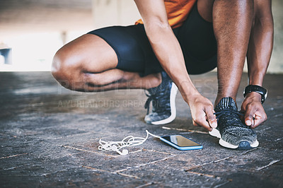 Buy stock photo Cropped shot of a man tying his shoelaces during a workout against an urban background