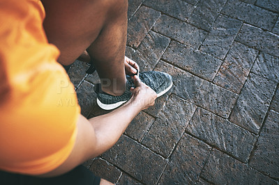 Buy stock photo Cropped shot of a man tying his shoelaces during a workout against an urban background