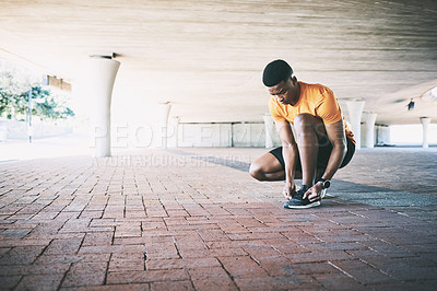 Buy stock photo Shot of a young man tying his shoelaces during a workout against an urban background