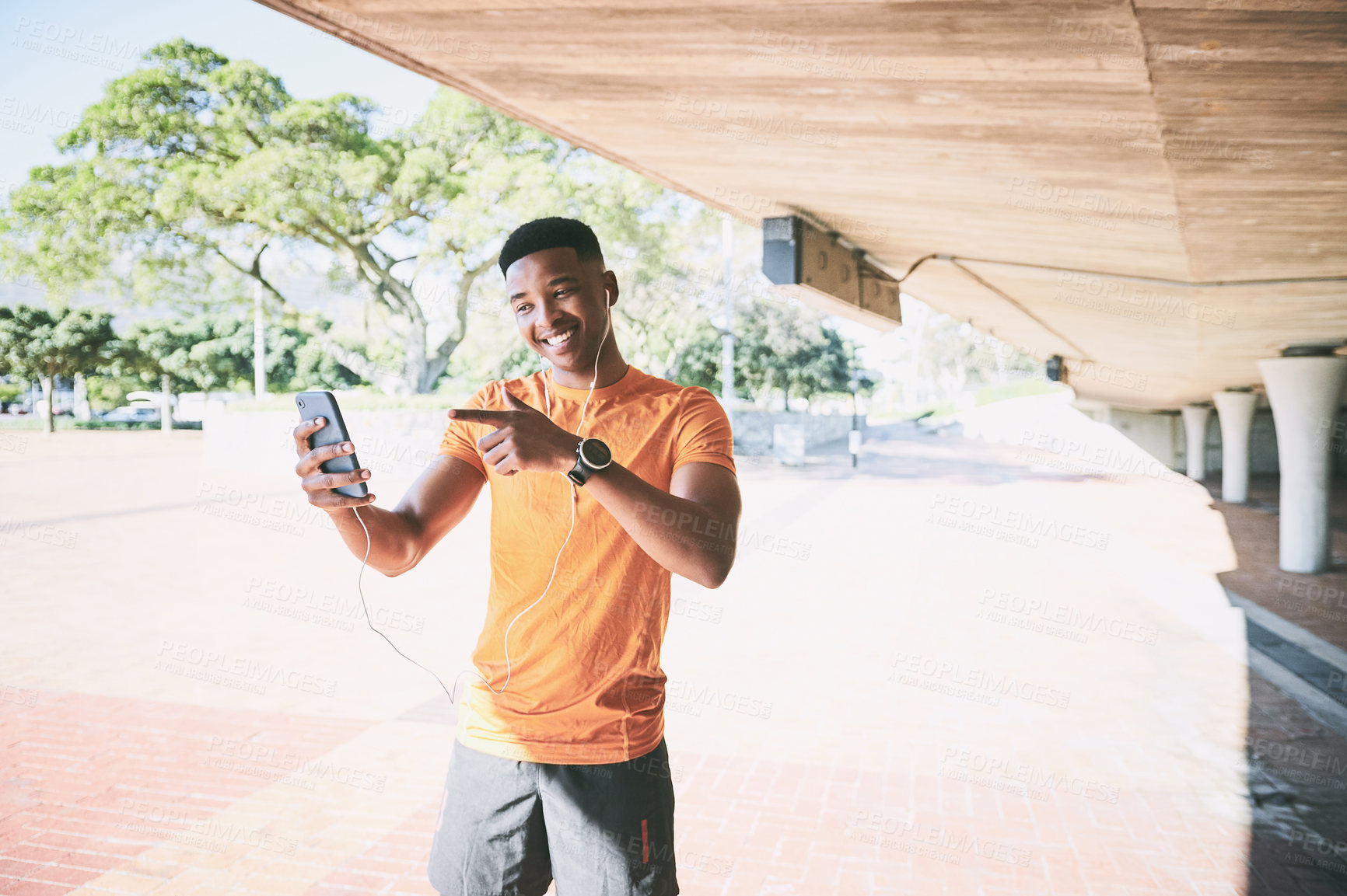 Buy stock photo Shot of a young man using a smartphone and earphones during a workout against an urban background