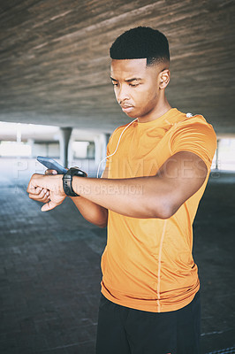 Buy stock photo Shot of a young man pairing his watch with a smartphone during a workout against an urban background