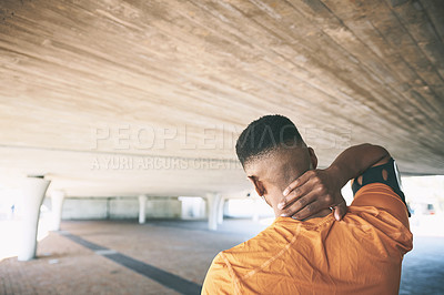 Buy stock photo Rearview shot of a young man experiencing neck pain while working out against an urban background